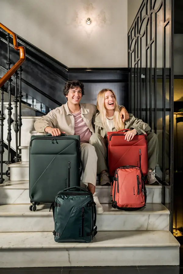 Pareja sentada en una escalera con maletas y mochilas de la nueva colección Canadá